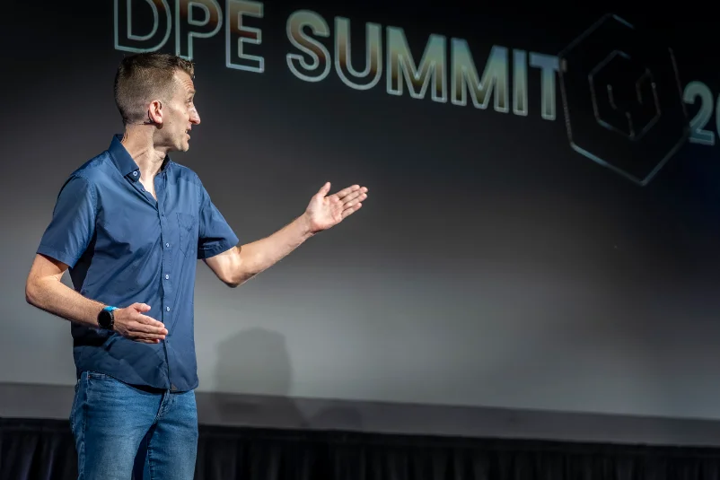 Speaker presenting in front of the DPE Summit backdrop